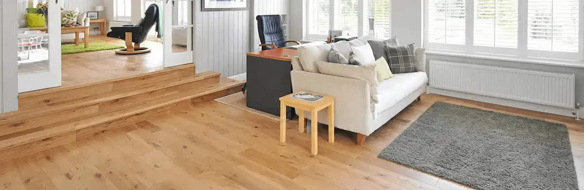 A modern living room with professionally installed laminate flooring, a beige sofa, a small side table, a gray rug, and large windows with white shutters in Lakeland, FL